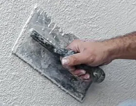 construction professional applying a layer of traditional cement-based stucco to an exterior wall using a trowel